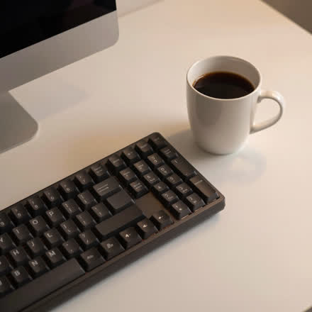 Xícara de café ao lado de um teclado, em mesa limpa.